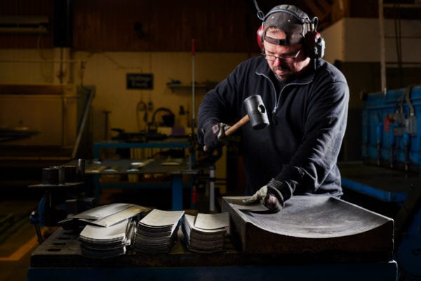 Skillinge Emalj emaljskylt - Robert kupar de valsade plåtarna med gummiklubba. Gjutjärnsformen kommer från gamla Kockums i Ronneby.